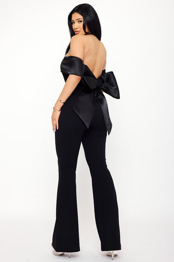 Black off-the-shoulder formal jumpsuit with a large satin back bow for a chic, elegant evening look from Boutinie.