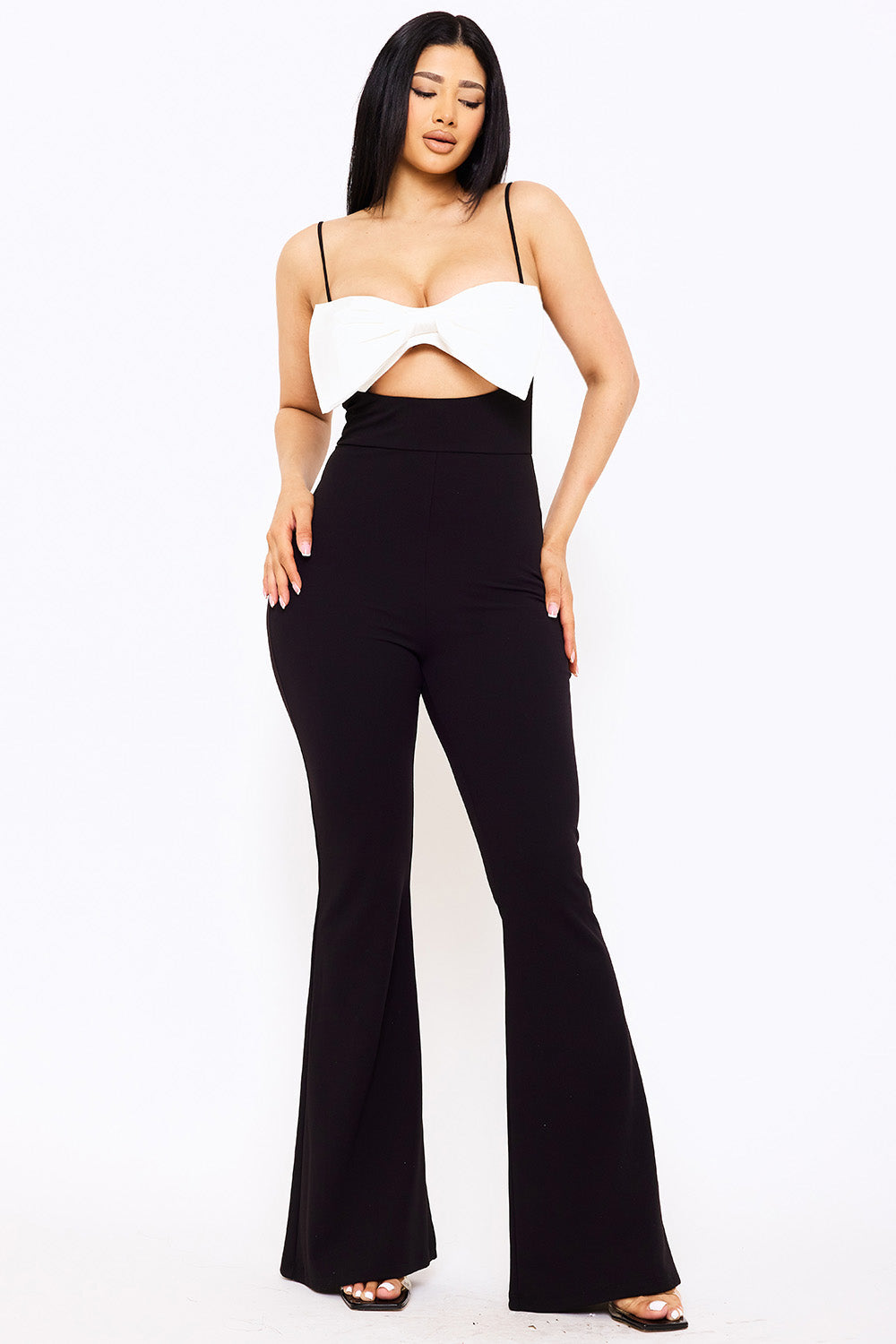 Model wearing a black jumpsuit with a white bow-detail bodice, spaghetti straps, and flared legs for a chic night out.