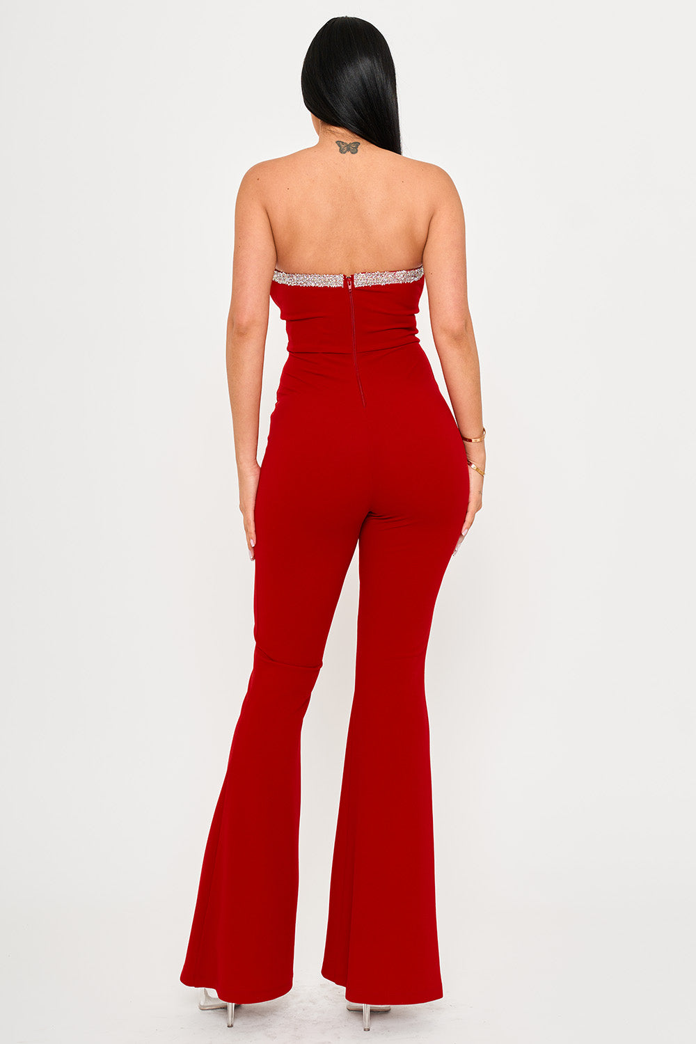 Back view of a red strapless jumpsuit featuring a sparkling rhinestone trim for formal evening events.