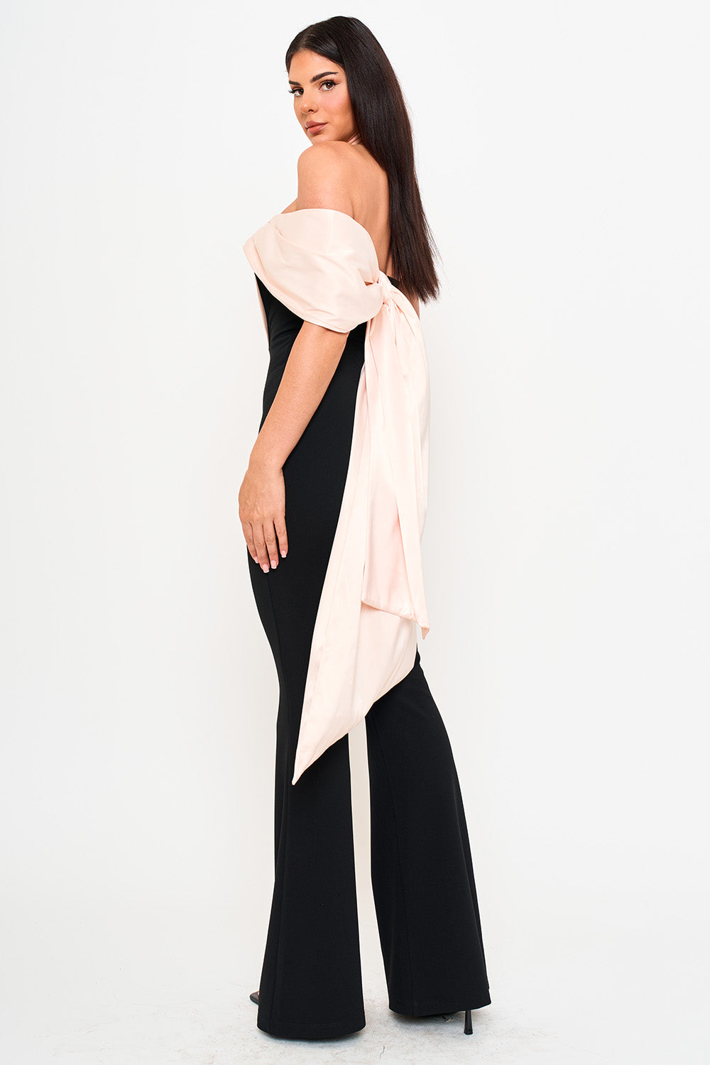 Black off-shoulder jumpsuit with blush pink satin bow detail for an elegant formal event.
