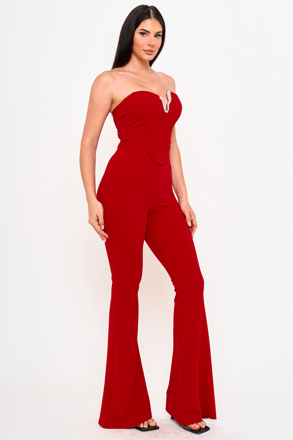 Model wearing a strapless red jumpsuit with a sweetheart neckline and rhinestone detail, perfect for evening wear.