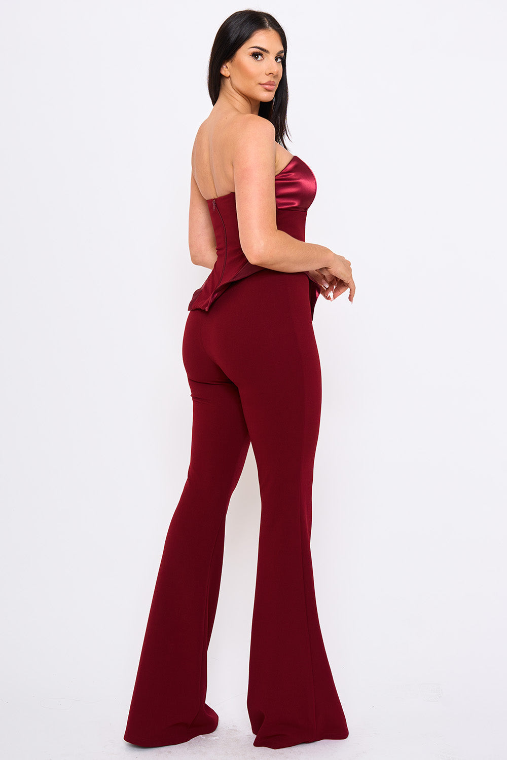 Model wears a chic burgundy strapless peplum jumpsuit with satin bodice and flared trousers for a formal event.