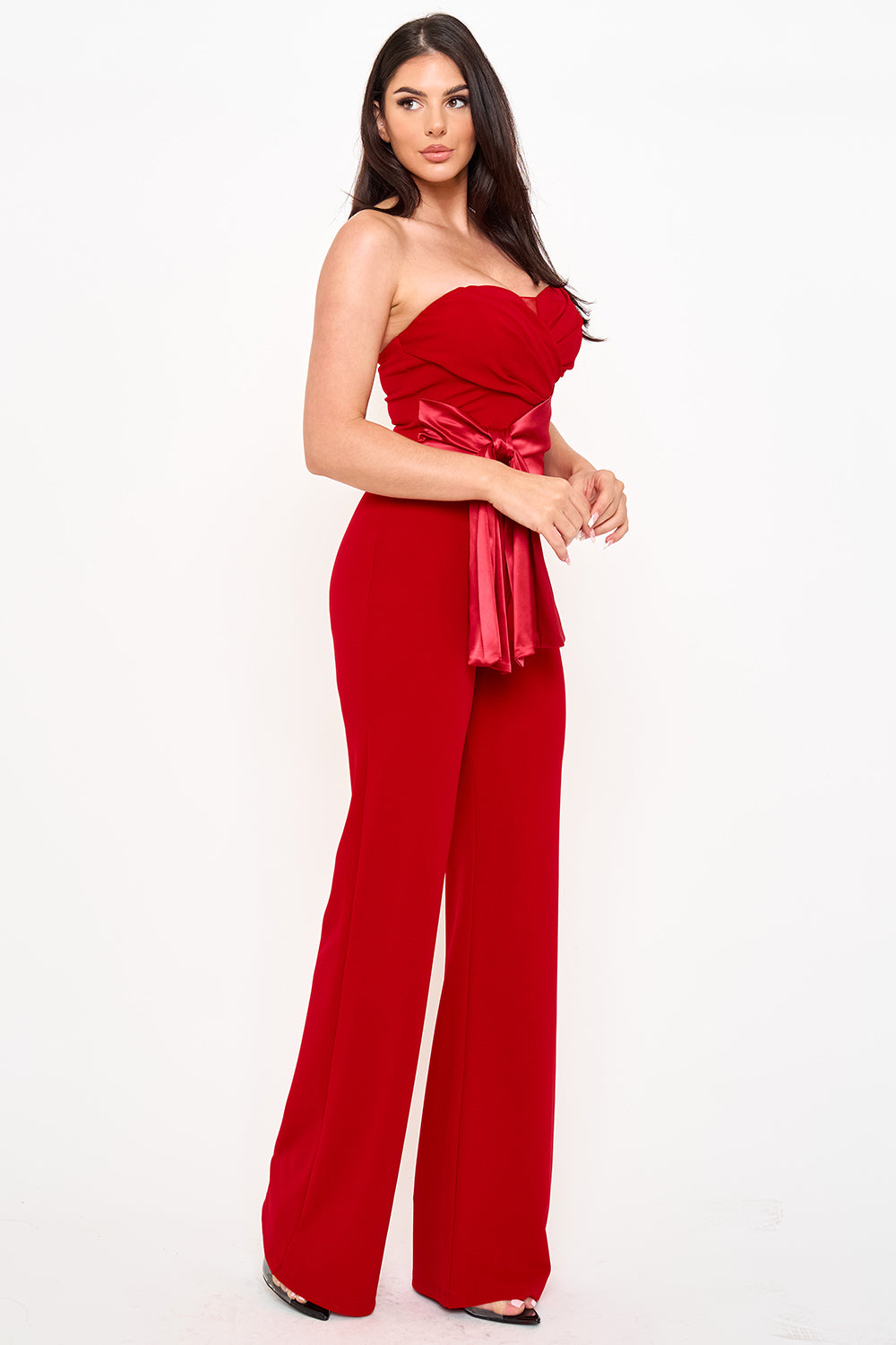 Red strapless jumpsuit by Boutinie featuring a ruched bodice, satin waist tie, and wide-leg silhouette for evening.