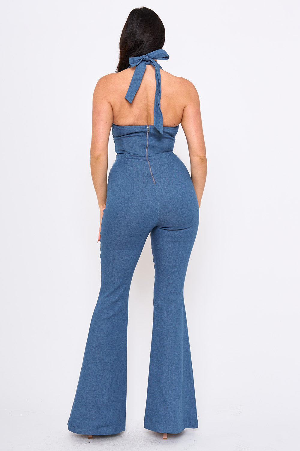 Back view of a blue denim halter jumpsuit with a tie-neck, zip back, and flared legs for a chic casual look.