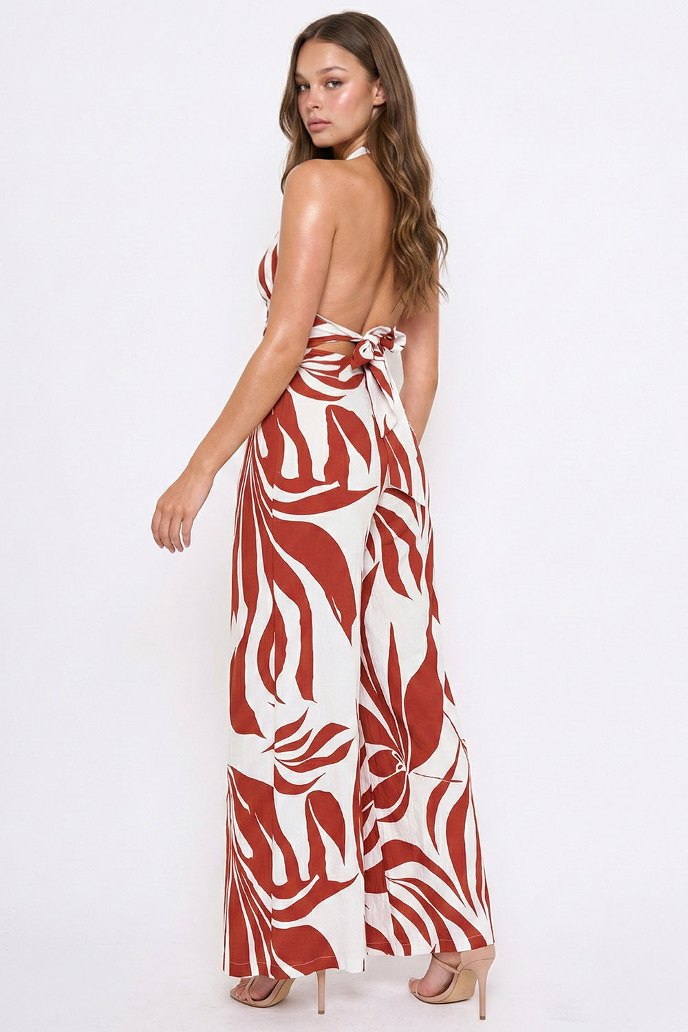Back view of a chic rust and cream leaf-print open-back halter jumpsuit, perfect for a stylish summer occasion.