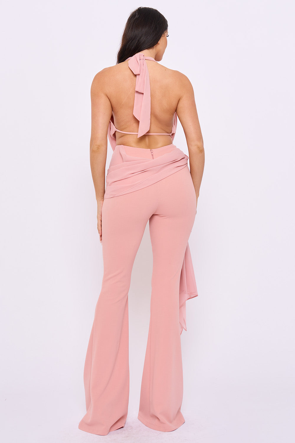 Dusty pink halter-neck jumpsuit with a backless design, draped waist detail, and flared legs for a chic evening look.