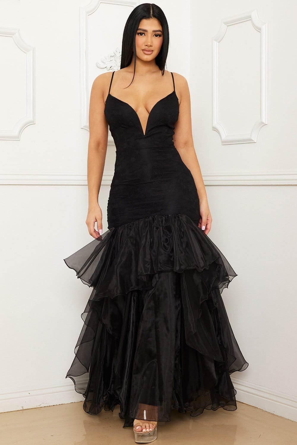 Model wearing a black lace mermaid evening gown with a plunging neckline, spaghetti straps, and tiered organza skirt.