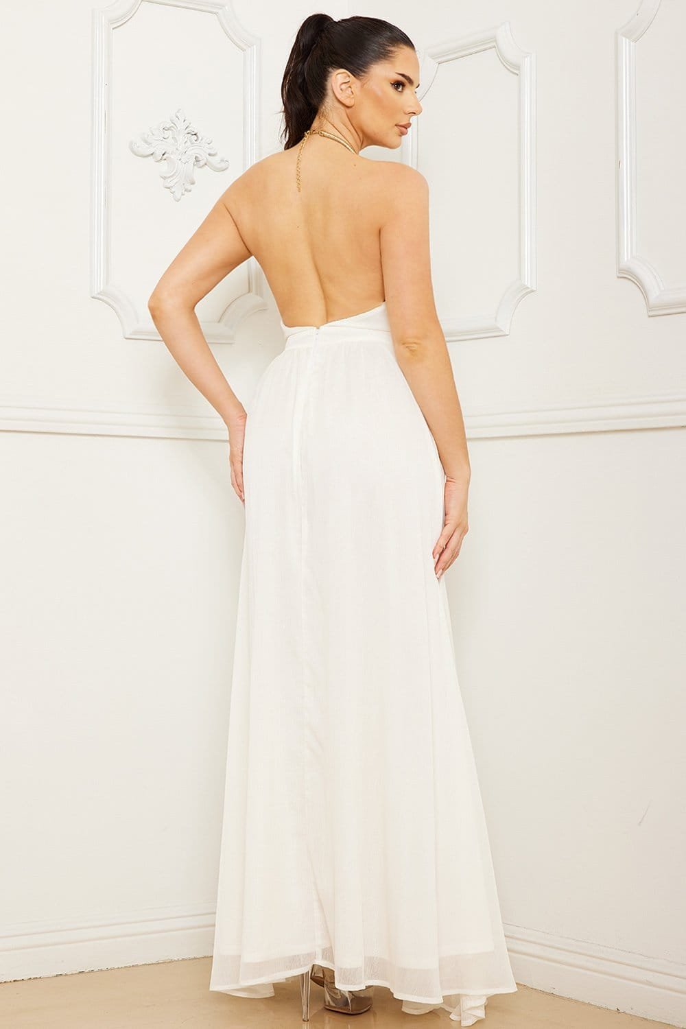 Elegant white maxi dress by Boutinie featuring a backless halter neck and flowing silhouette for formal occasions.