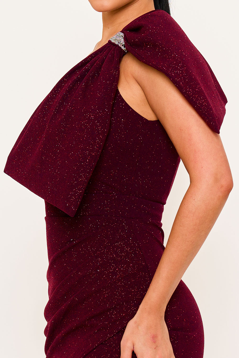 Burgundy glitter evening dress with one-shoulder drape detail, crystal brooch, and form-fitting silhouette.
