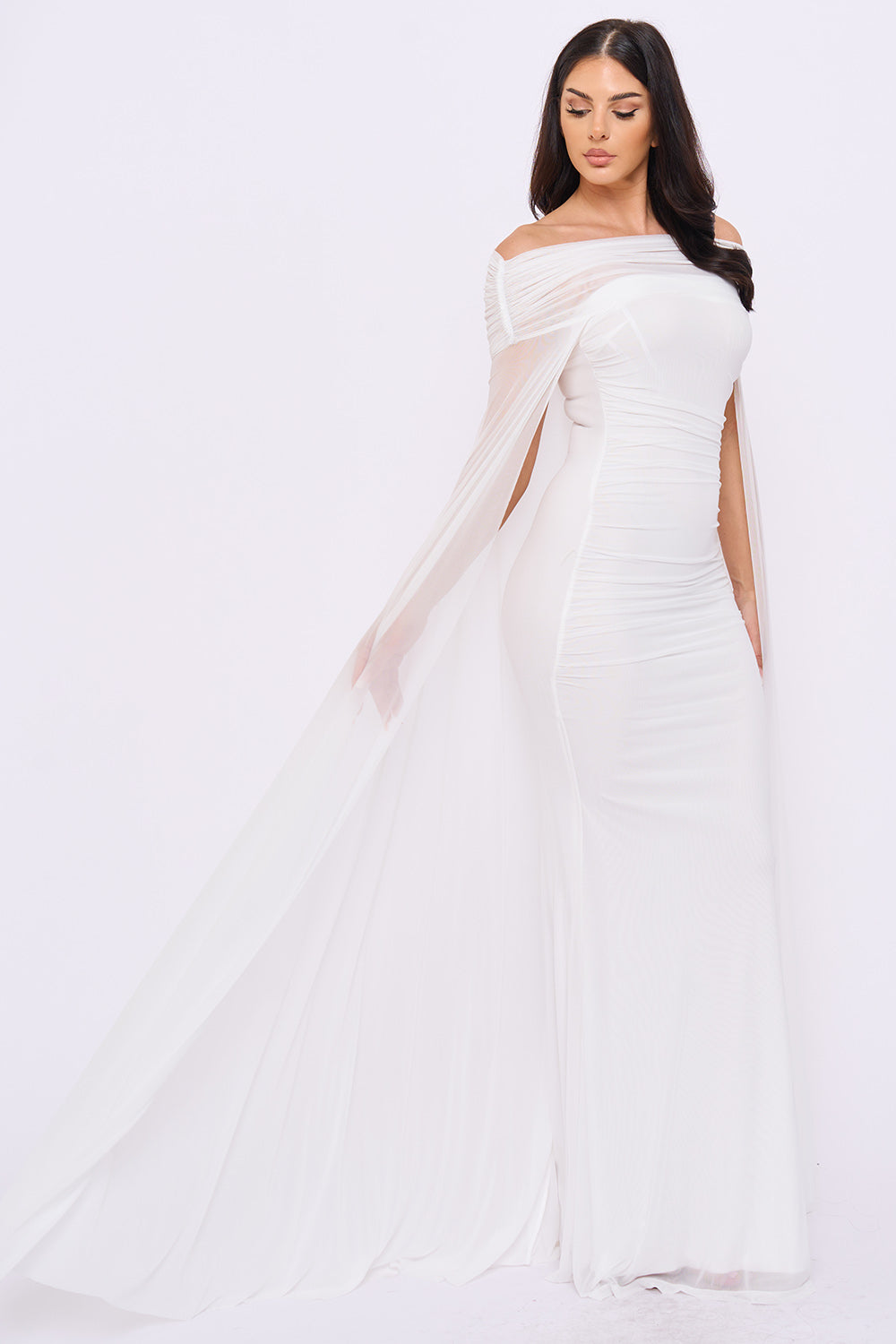 White off-shoulder ruched maxi gown with elegant sheer cape sleeves, perfect for formal events from Boutinie.