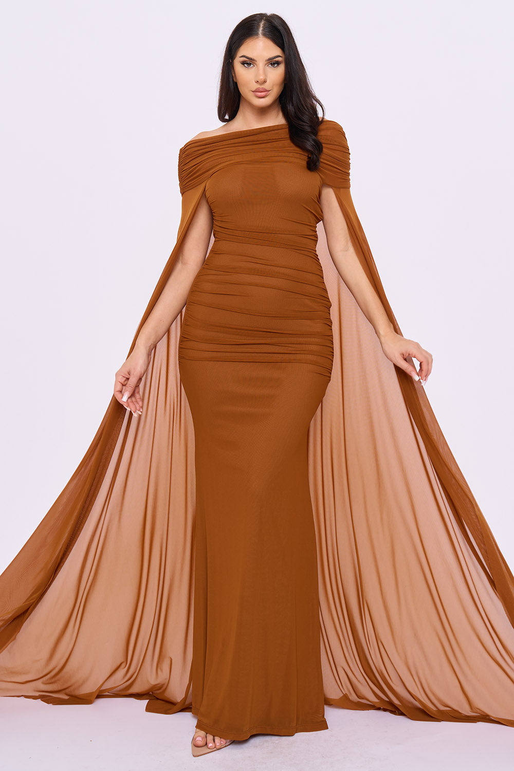 Model wearing a mocha ruched off-shoulder evening gown with dramatic sheer cape sleeves from Boutinie.
