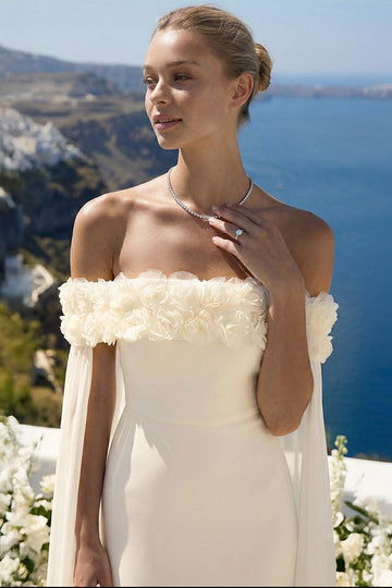 Ivory off-shoulder wedding gown featuring 3D floral neckline detail and flowing cape sleeves by Boutinie.