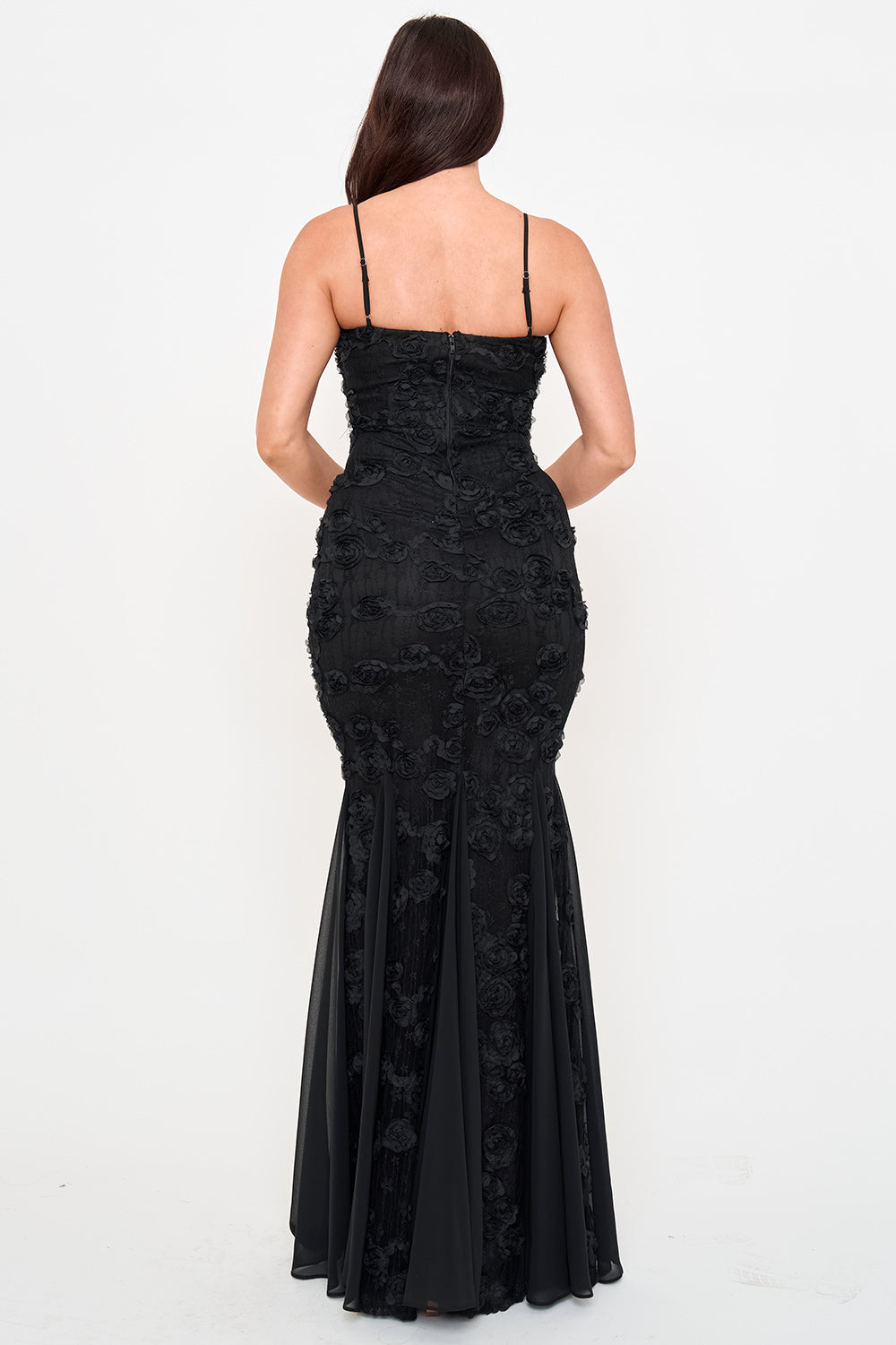 Back view of a black floor-length mermaid gown with 3D floral lace appliqué, spaghetti straps, and chiffon hem.